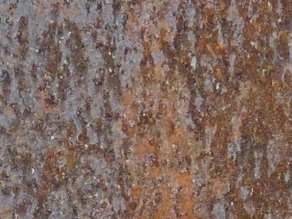 Rough blue rust texture, with various dark streaks and spots, covering a metal surface.